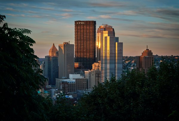 The Pittsburgh skyline is shown in the evening through trees